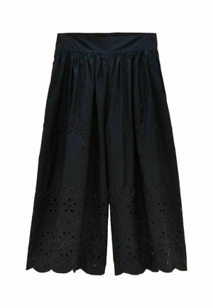 Frau trägt marineblaue, weit geschnittene, knöchellange Hose mit floraler Cut-out-Stickerei und braune Sandalen mit Absatz und Schnallen.