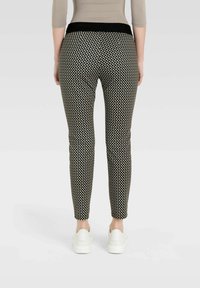 Schwarz-weiße gemusterte Hose mit einem breiten schwarzen Bund, schlanker Passform und knöchellangem Design, kombiniert mit weißen Sneakers.