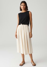 Zwarte mouwloze top en ivoorkleurige midi rok met een elastische trekkenband in de taille. Eenvoudig ontwerp, lichtgewicht stof en platte sandalen maken de outfit compleet.