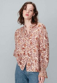 Blouse à motif floral en crème avec des accents rouille et or, dotée d'un devant à boutons, de manches longues et d'un design détaillé sur les poignets.