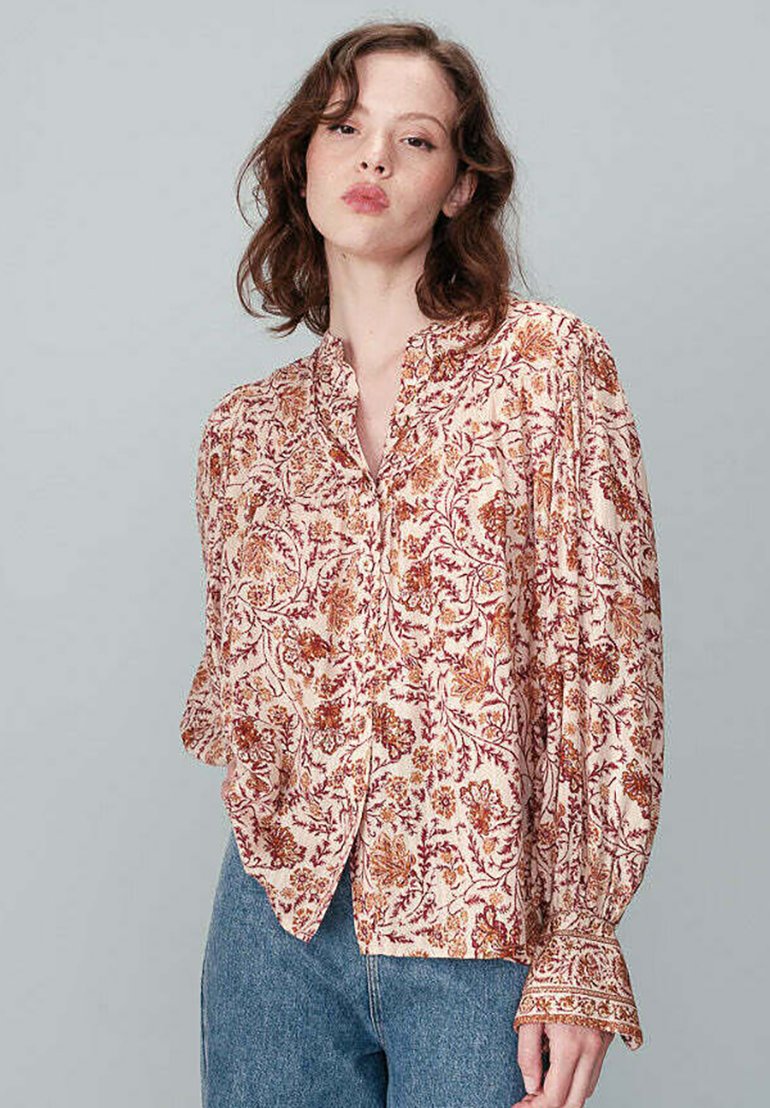 Blouse à motif floral en crème avec des accents rouille et or, dotée d'un devant à boutons, de manches longues et d'un design détaillé sur les poignets.