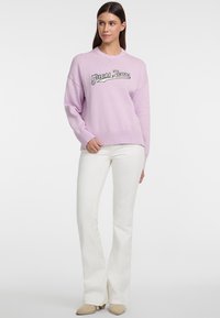 Hellblau übergroßer Pullover mit gerippten Bündchen und Saum, mit weißem und schwarzem "Guess Jeans"-Stickerei auf der Vorderseite. Kombiniert mit weißen Schlaghosen.