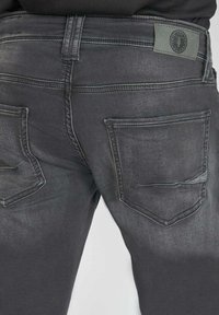 Des jeans en denim gris présentent une coupe ajustée, deux poches arrière et un délavage subtil. Inclut une étiquette texturée à la taille.