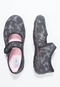 Svarta tygskor med en texturerad yta, rosa inredning och ett kardborreband. Har en flexibel gummisula med blommotiv.