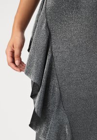Pilkas, blizgantis audinys, su sluoksniuotais ruffles iš vienos pusės. Tekstūra lygi su blizgiu paviršiumi, sustiprinančiu elegantišką dizainą.