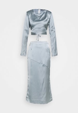 Ensemble deux pièces en satin bleu clair avec haut court à manches longues et jupe taille haute longueur cheville avec détail de couture diagonale.