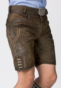 Shorts en cuir marron avec broderies décoratives sur le côté, dotés de boutons en argent et d'un design ajusté. Surface texturée avec un look classique.