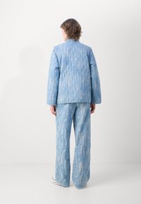 Giacca blu trapuntata con un motivo testurizzato e pantaloni a gamba larga coordinati. Il tessuto ha una superficie morbida e dettagli di design sottili.