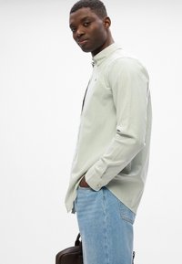 Γαλανόριζος πουκάμισο με γιακά, μακριά μανίκια και χαλαρή εφαρμογή, συνδυασμένο με ανοιχτόχρωμες τζιν παντελόνες και καφέ τσάντα.