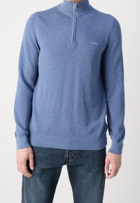 Blauer Reißverschluss-Pullover mit hohem Kragen, strukturiertem Strickmuster und gerippten Bündchen und Saum. Minimalistisches Markenlogo auf der Brust.