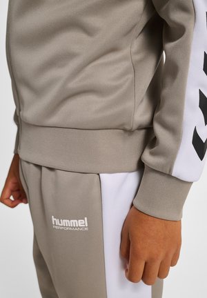 Gråt sportstræningssæt med struktureret stof, hvide detaljer på ærmer og bukser samt en logo vist foran.