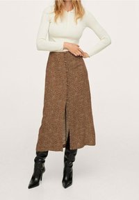 Falda midi marrón con un patrón de manchas, con una abertura frontal y detalle de botones, combinada con botas negras hasta la rodilla y una parte superior blanca de canalé.