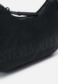 Sac à main texturé noir Steve Madden avec forme incurvée, fermeture éclair sur le dessus et nom de marque embossé sur le devant.