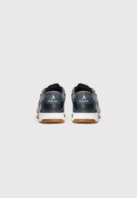 Pair of black slip-in sneakers with white midsoles and brown outsoles shown from the back on a white background.