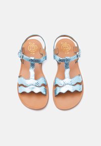 Παιδικά σανδάλια με μεταλλικές μπλε, κυματιστές λουρίδες και ταμπά σόλες με αγκράφες στον αστράγαλο, τοποθετημένα δίπλα δίπλα σε λευκό φόντο.