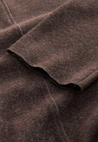 Brązowy sweter o prążkowanej strukturze. Długie rękawy i delikatnie falbaniaste mankiety. Materiał wydaje się miękki i lekko puszysty.