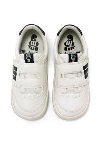 Zapatos de cuero blancos con acentos negros, que cuentan con correas de Velcro, un interior acolchado y etiquetas impresas de pie izquierdo/derecho en su interior.