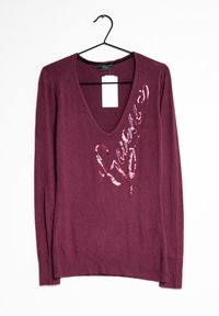 Sweater bordeaux à manches longues avec un décolleté en V profond et un logo "Guess" en sequins sur le côté gauche. Matière douce et détails de bas en côtes.