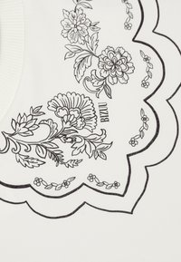 Witte kleding met zwarte bloemillustraties rondom een golvende halslijn. Het ontwerp bevat gedetailleerde bloemen, bladeren en kleine accenten.