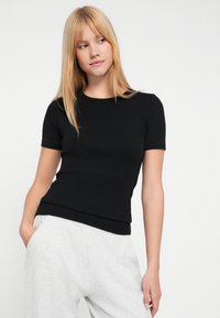 Czarny prążkowany t-shirt z krótkim rękawem i okrągłym dekoltem, zestawiony z jasnoszarymi spodniami dresowymi. Gładka faktura, dopasowany krój.