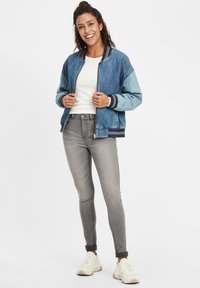 Denim bomber jakna u svijetloplavoj i tamnoplavoj boji, s rebrastim manžetama i rubom. Nošena preko bijele košulje u kombinaciji s sivim uskim trapericama i svijetlim tenisicama.