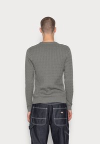 Grå kabelstickad tröja med långa ärmar och rund halsringning, tillverkad av ett mjukt stickat material. Har ribbade manschetter och fåll.