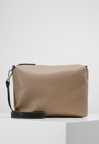 Pochette rectangulaire en cuir beige avec une bandoulière noire détachable posée sur une surface blanche.