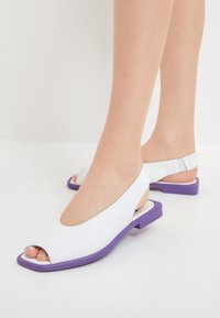 Sandali slingback open-toe in pelle bianca con tacco a blocco viola, caratterizzati da un design elegante e dettagli testurizzati.