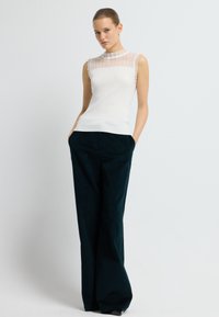 Hvid r ribbet ærmeløs top med gennemsigtig tekstureret panel ved udskæringen, parret med mørkegrønne brede bukser. Glat stof og skræddersyet pasform.