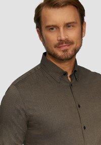 Braun gemustertes Hemd mit Button-Down-Kragen, das kleine Karos und schwarze Knöpfe aufweist und aus strukturiertem Stoff gefertigt ist.