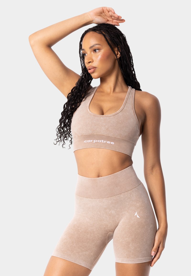Béžová sportovní podprsenka a šortky s vysokým pasem vyrobené z jemného materiálu. Obsahují logo značky na pase a mají přiléhavý střih pro volný pohyb.