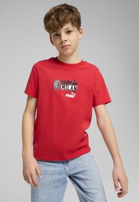 Červené tričko s krátkym rukávom s grafickým potlačou "Forza Milan" a logami, vyrobené z bavlny, v kombinácii s svetlo modrými džínami.