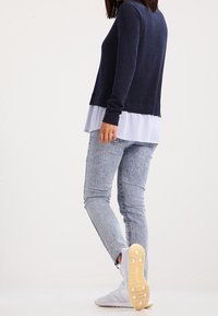 Navy long-sleeve sweater layered over a light blue striped shirt, paired with light blue jeans and white sneakers with a textured sole.
