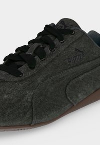 Σκούρο γκρι υφασμάτινο αθλητικό παπούτσι Puma με μαύρα κορδόνια, εμφανές λογότυπο στο πλάι και στη γλώσσα, και καφέ σόλα.