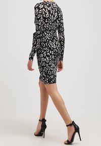 Svart klänning med leopardmönster, långa ärmar, figurnära passform, kortare längd till mitten av låren, kombinerad med svarta högklackade skor.