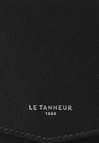Portafoglio in pelle nera con superficie testurizzata; presenta il nome del marchio impresso "LE TANNEUR" e "1898" in bianco. Dettaglio di cucitura sottile.
