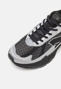 Black and silver athletic shoes featuring mesh overlays, textured accents, rounded toe, and black laces against a white background.