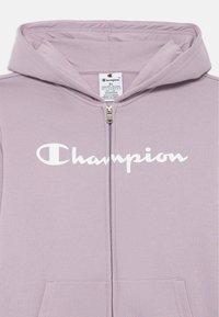 Levanduľová mikina na zips s bielym logom "Champion" na hrudi, vybavená kapucňou, prednými vreckami a mäkkou textúrou tkaniny.
