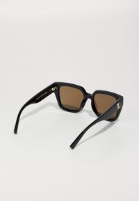 Sorte solbriller med geometrisk ramme, brune linser og en blank finish. Utsmykket med en liten gulllogo på stengene.