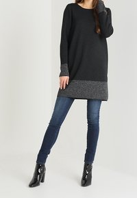 Pull tunique noir avec un accent gris au bas et aux manches, associé à un jean bleu foncé et des bottines noires brillantes. Texture lisse.