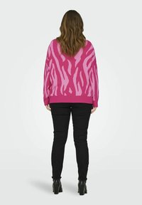 Pulover roz cu un model cu dungi de zebra pe spate, asociat cu pantaloni negri. Puloverul are o croială lejeră și mâneci lungi.