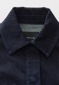 Camicia di denim blu scuro con colletto strutturato, dotata di una patta con bottoni frontali e una leggera lucentezza. L'etichetta riporta "OPUS."