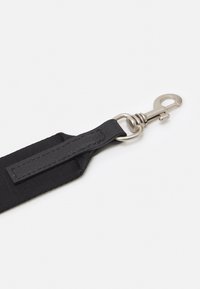 Svart nylonrem med en strukturerad yta, utrustad med en metallklämma och läderdetaljer för fäste. Enkelt, funktionellt design.