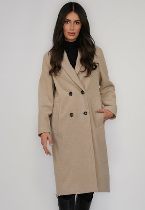 Beżowy dwurzędowy płaszcz wykonany z miękkiego materiału, z dużymi guzikami, dwoma przednimi kieszeniami i kołnierzem z wycięciem. Projekt uzupełniają długie rękawy.
