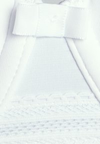 Nahaufnahme von weißem Stoff mit gerippter Struktur, Schleife und filigranen Spitzenmustern auf einem Kleidungsstück.