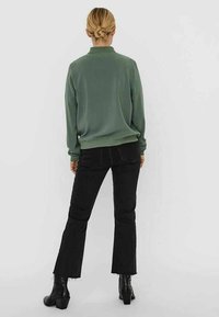 Green fleece pullover with a high neckline and ribbed cuffs, paired with black flared jeans and ankle boots with a chunky heel.