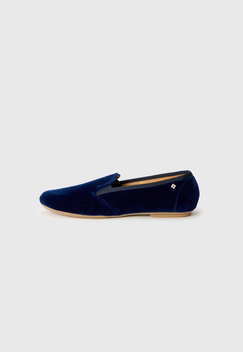 Chaussure à enfiler en velours bleu marine avec un bout arrondi et des accents élastiques. Dispose d'une semelle plate de couleur claire pour le confort. Pas de motifs visibles.