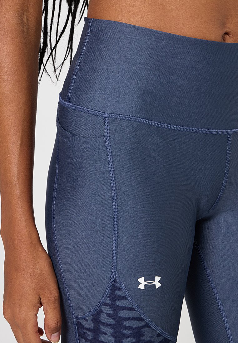 Acercamiento de una persona que lleva mallas deportivas de talle alto en color azul marino con bolsillos laterales y un logo de Under Armour en blanco.