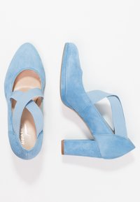 Escarpins en suédine bleue avec un bout rond et un design à brides croisées. Le talon est épais, offrant stabilité et soutien.