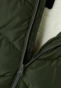 Giacca imbottita verde oliva con design a soffietto, dotata di una cerniera argentata. La fodera interna ha una texture morbida e pelosa.